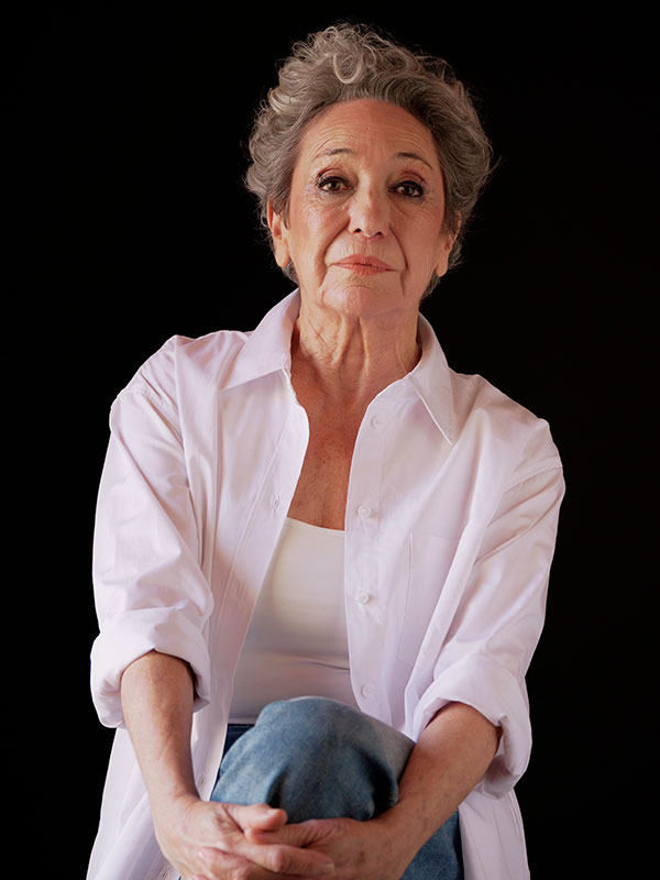 Retrato de la actriz Luisa Gavasa, con pelo gris corto y camisa blanca, sobre fondo negro.